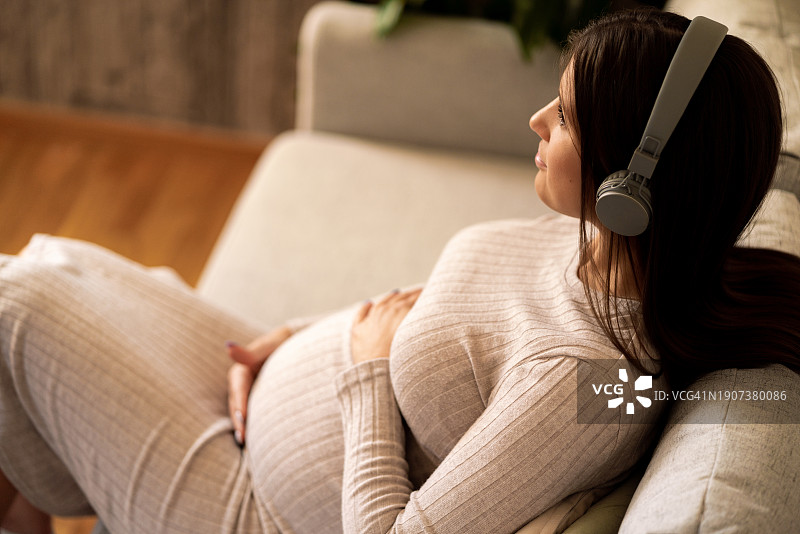 戴着耳机在家放松的孕妇图片素材