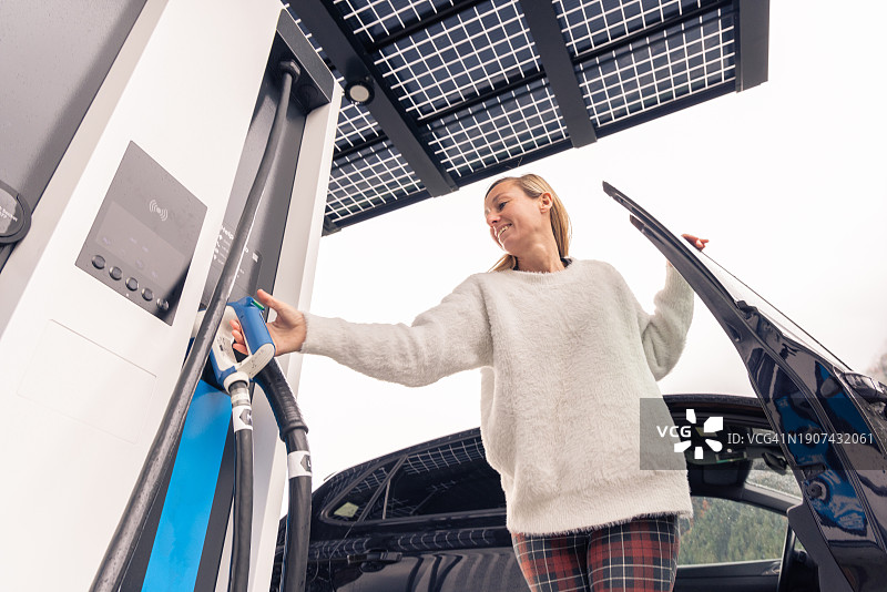 女子在公共太阳能充电站为电动汽车充电图片素材