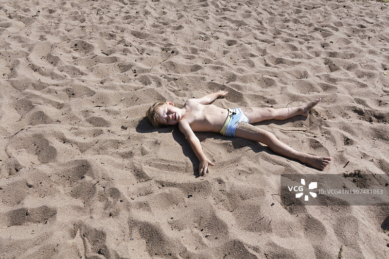 一个小男孩躺在湖边或河边的沙滩上，身上沾着小沙粒图片素材