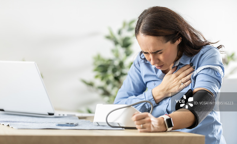 年轻女人在感到胸闷后用血压监测仪测量血压图片素材
