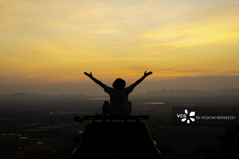 站在乡村景观汽车顶上伸出双臂的年轻男人图片素材