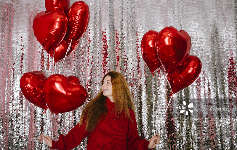 快乐的年轻女子在家中拿着气球站在亮片窗帘前图片素材