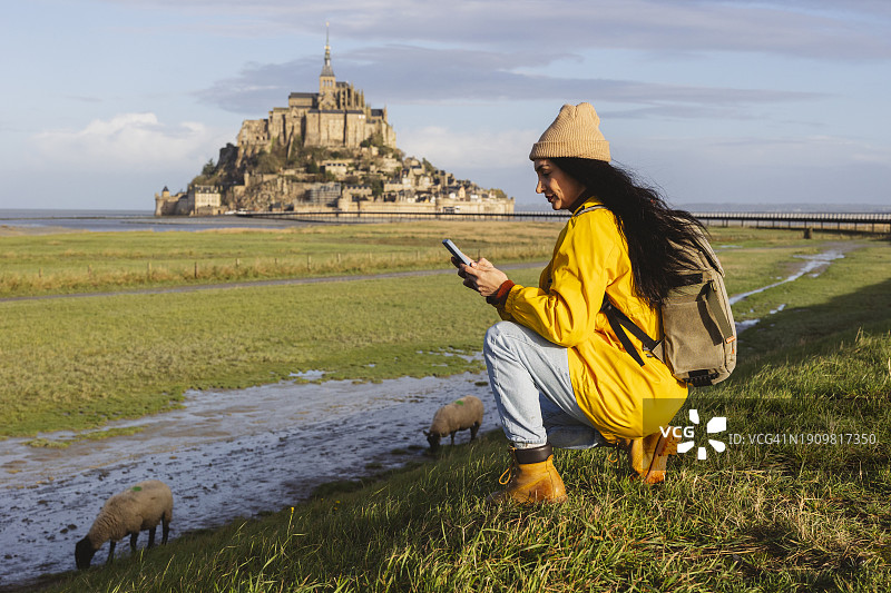 在草地上放羊时使用智能手机的女人图片素材