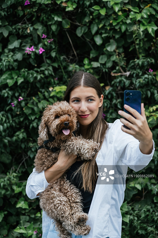 微笑的女人在植物前与贵宾犬自拍图片素材