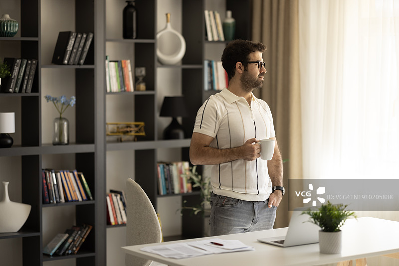 在办公室喝咖啡时使用笔记本电脑的沉思商人图片素材