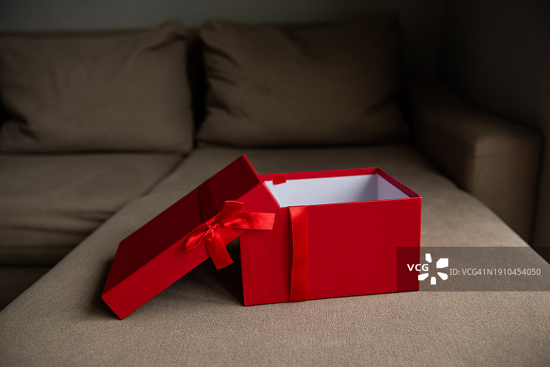 鲜红色的礼品盒，带缎带蝴蝶结，空置在米色沙发上，暗示着惊喜礼物样机图片素材