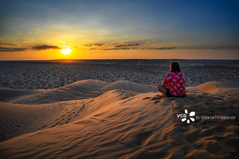 日落时分，女子坐在沙滩上看天空的背影图片素材