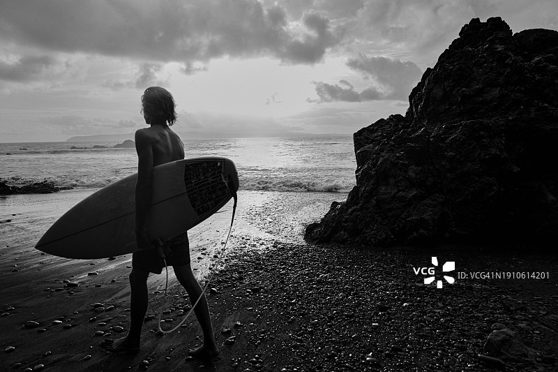 一个年轻的男性冲浪者走过海滩的背影图片素材