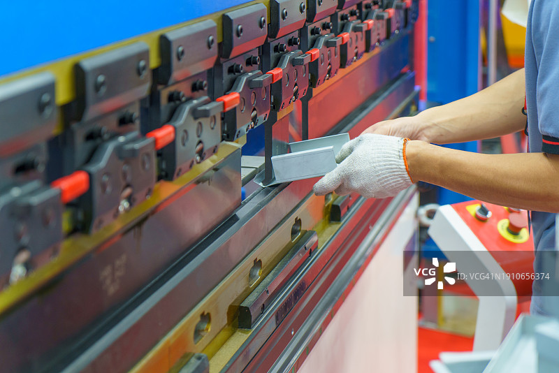 工人将金属板装载到数控同步液压折弯机上，工业金属加工机械图片素材