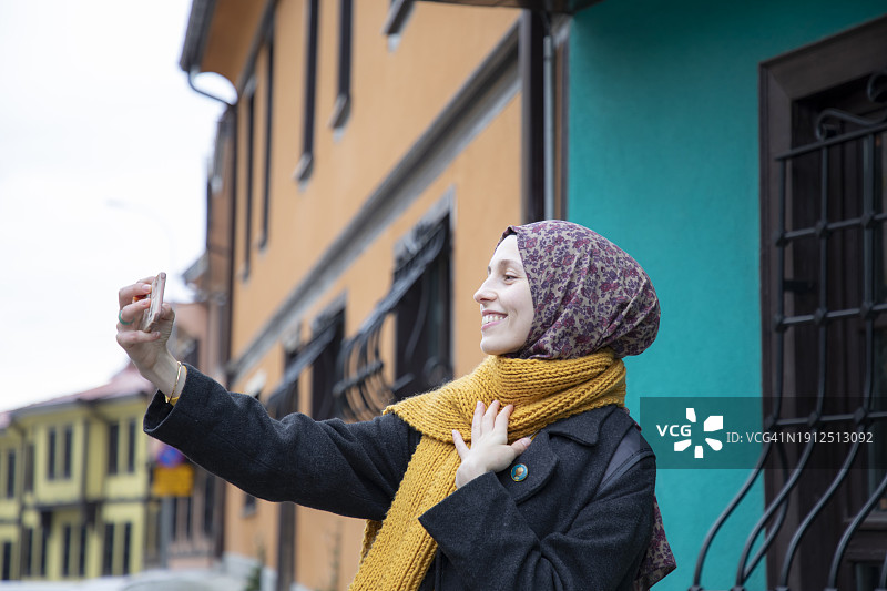 年轻的穆斯林女游客在埃斯基谢希尔历史悠久的奥敦帕扎勒房屋前自拍图片素材