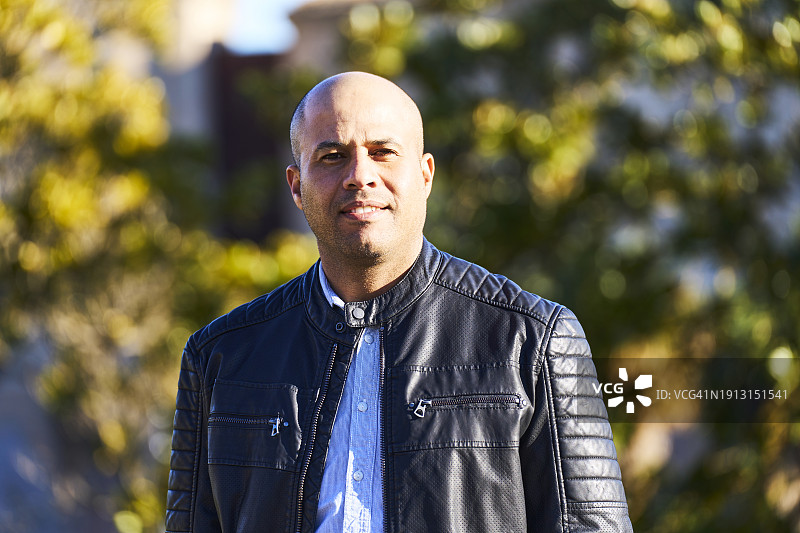 穿着皮夹克站在公园里微笑看着镜头的男子肖像图片素材