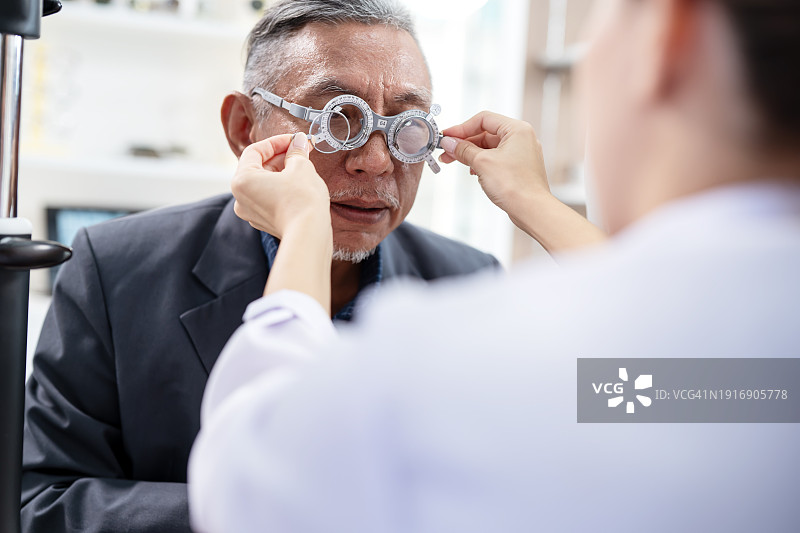 定期视力检查有益于老年人视力健康：女验光师在眼科诊所为亚洲老年患者检查眼睛，并调整焦距图片素材