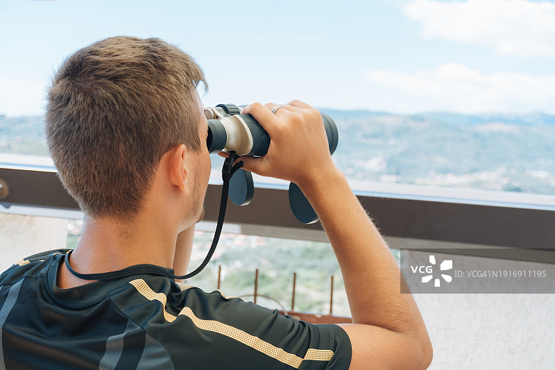 男子用双筒望远镜观看彩色群山全景图片素材