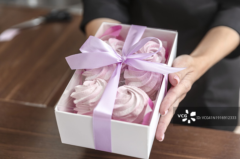 特写：女人的手在盒子上系丝带，用于客户订单。面包店厨师在厨房里烘烤糕点和蛋糕。小企业主和食品配送概念。图片素材