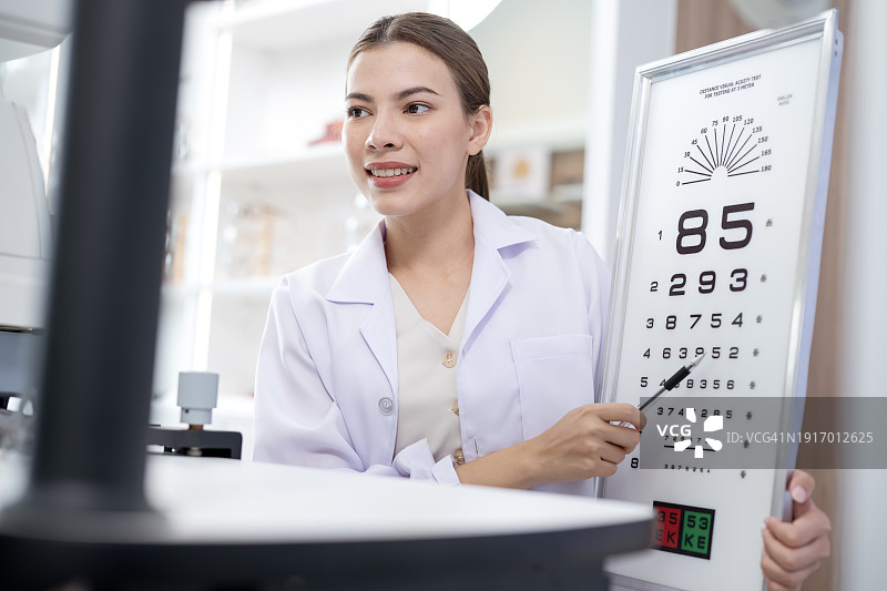 视力矫正可以提高日常生活质量。在眼科诊所，一名女验光师在眼科咨询期间指向视力表，让患者在阅读距离上进行测试图片素材
