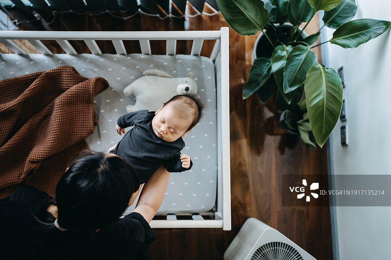 母亲怀抱中熟睡的可爱亚洲新生女婴俯视图。母爱、关怀和温柔，母性概念图片素材