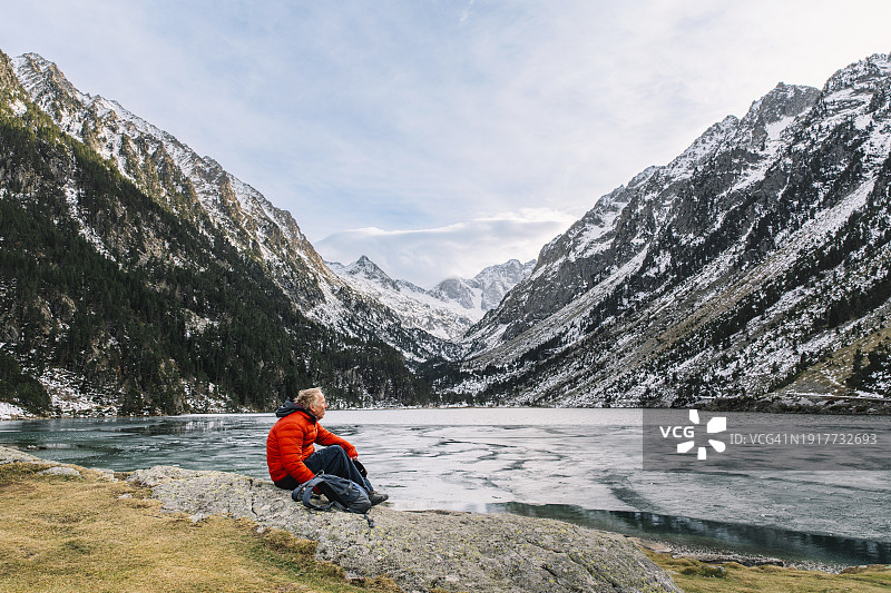 在一个晴朗的冬日，一位年长的男人眺望法国比利牛斯山脉壮丽的湖泊和山脉景观图片素材