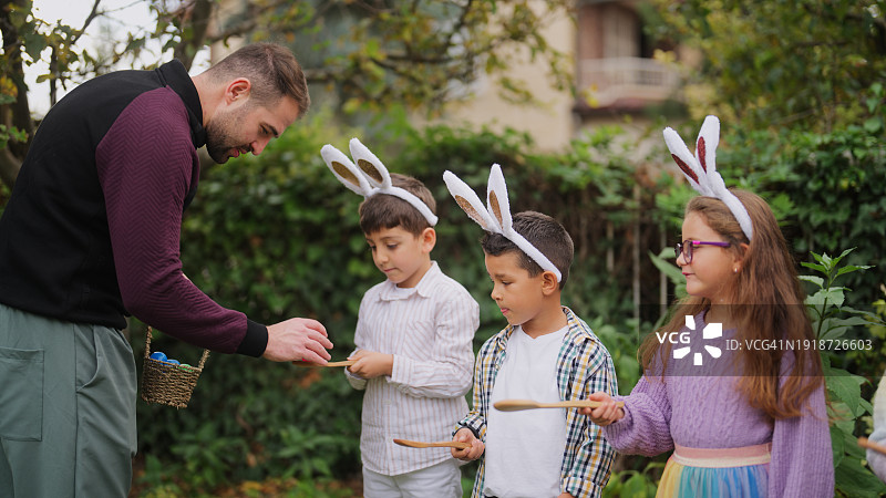 年轻男子向一群在户外玩耍的儿童讲解鸡蛋竞走比赛图片素材