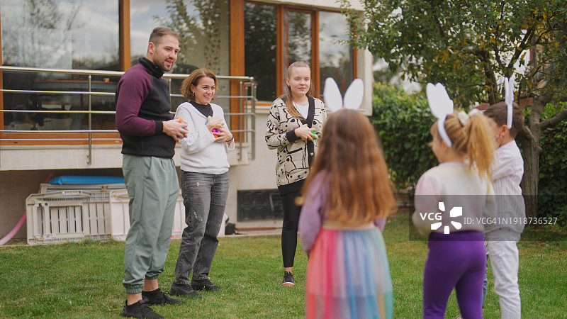 成年人在后院花园向孩子们讲解复活节彩蛋游戏图片素材