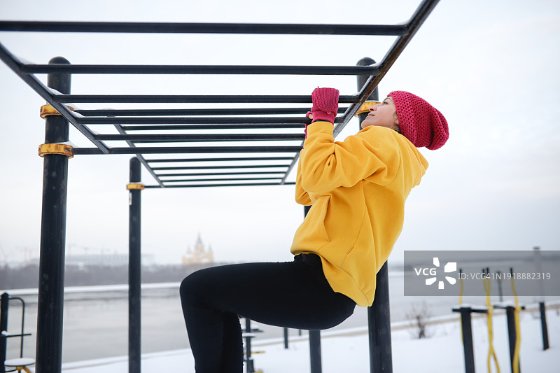 冬季锻炼：在寒冷气候的街头健身房做引体向上的苗条中年妇女，留白图片素材