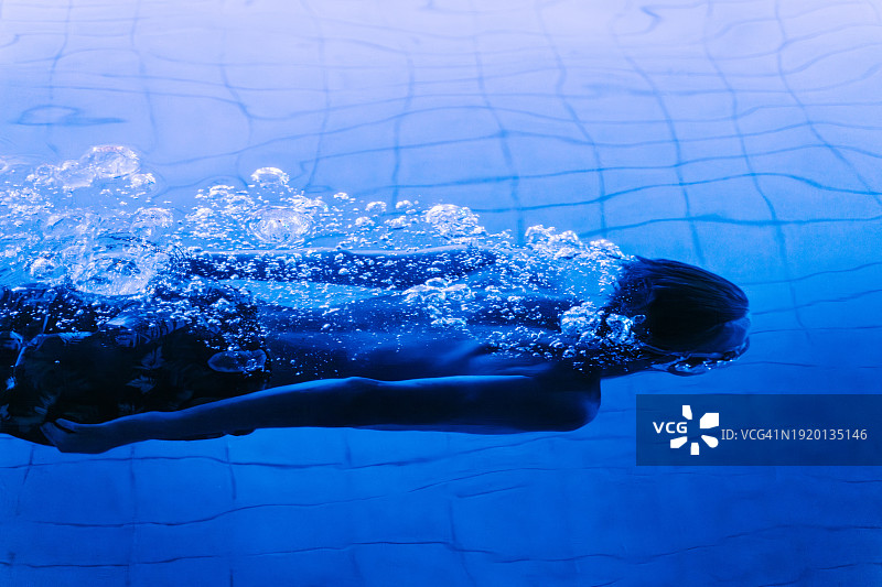 傍晚在游泳池中游泳的男子，霓虹灯光图片素材