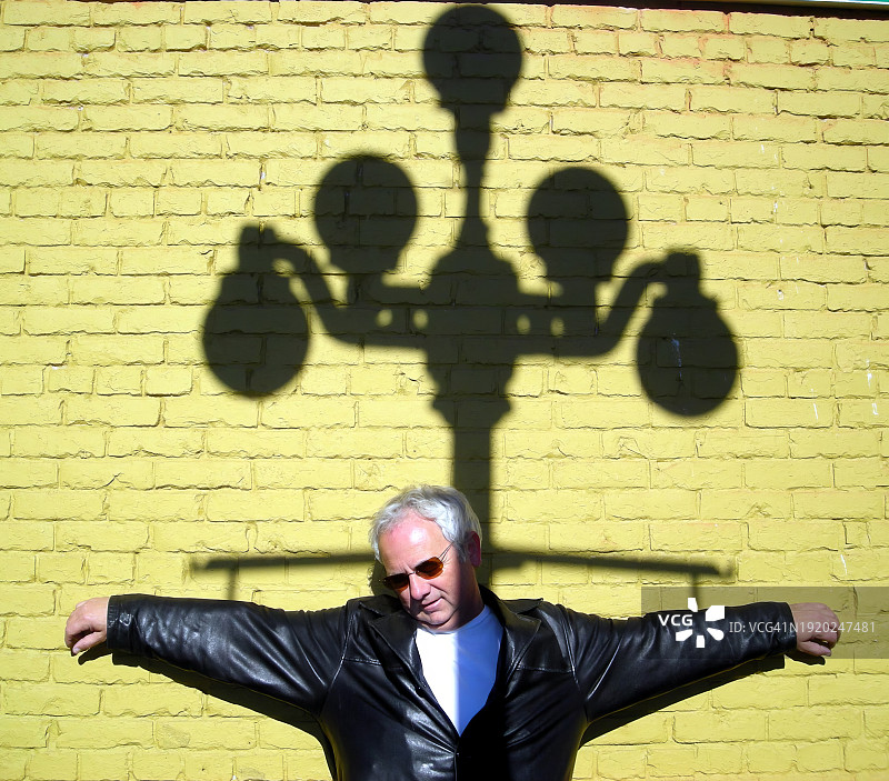 站在黄砖墙前，手臂伸向路灯阴影的男子图片素材
