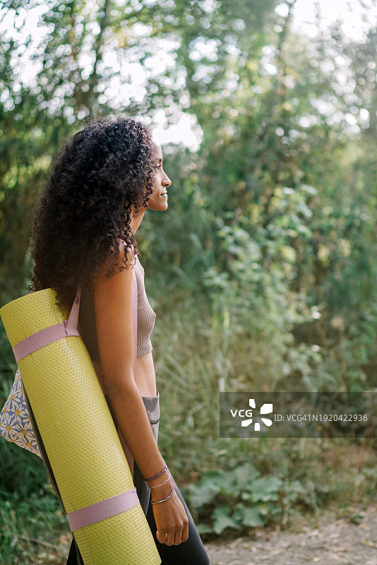 女子携带瑜伽垫靠在树旁的侧视图图片素材