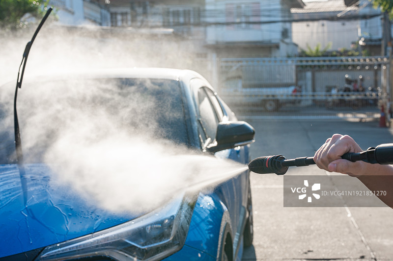 年轻的亚洲男子用水枪清洗汽车图片素材