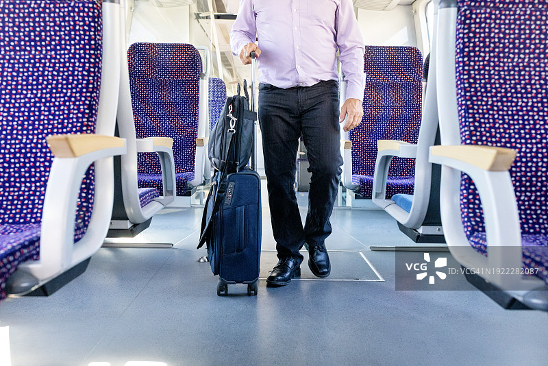 老年男人拖着行李箱走在火车车厢内的下半身视角图片素材