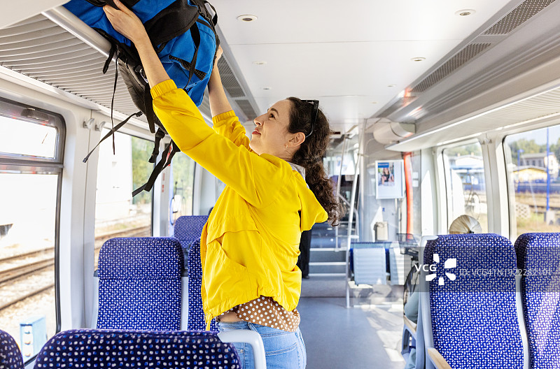 年轻女子将包放在火车车厢的行李架上图片素材