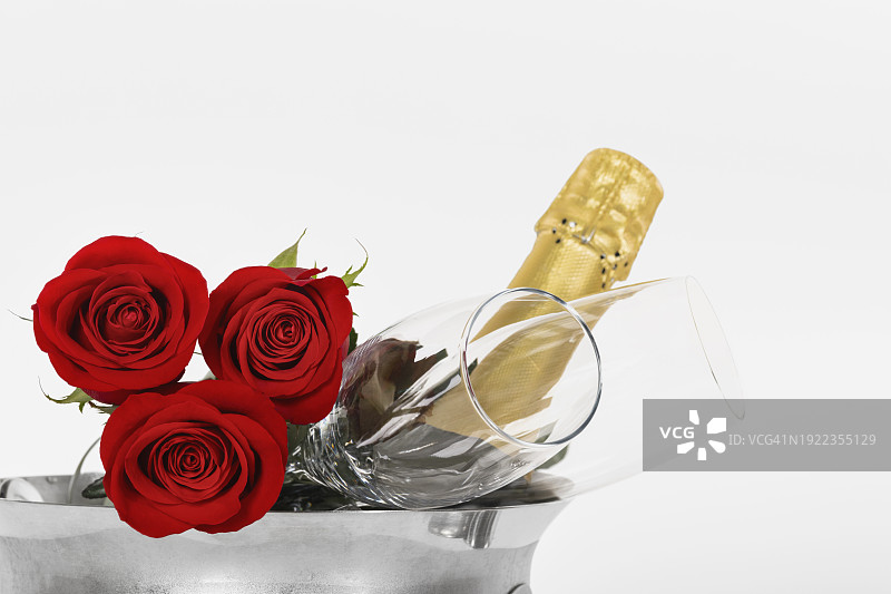 香槟酒瓶、香槟酒杯和鲜艳的红玫瑰：情人节和庆祝概念图片素材