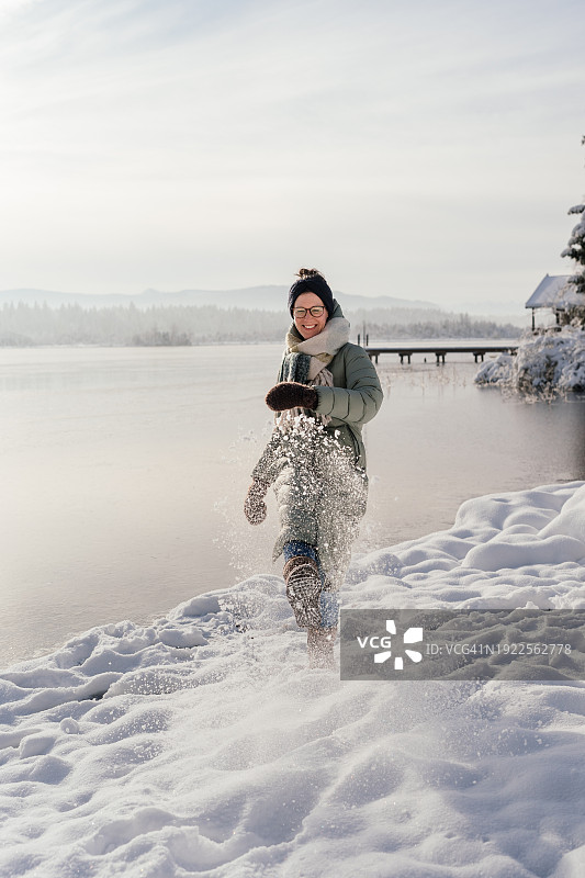 在冬天结冰的湖面上向镜头踢雪的女人图片素材