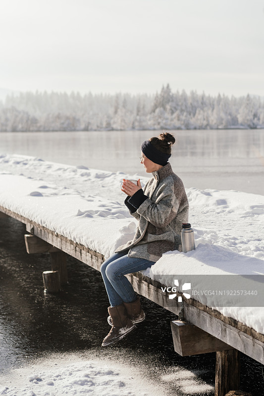 冬天坐在湖边桥上喝茶的女人图片素材