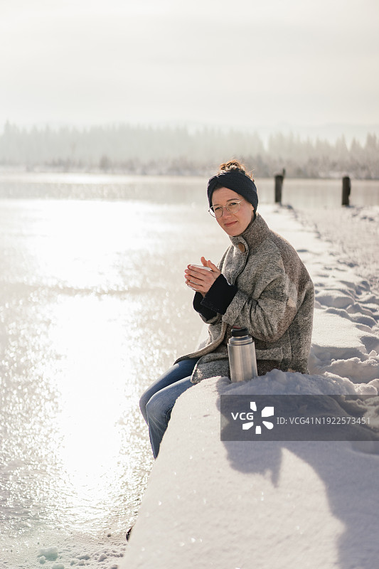冬天，坐在湖上桥上喝茶，看着镜头的女人图片素材