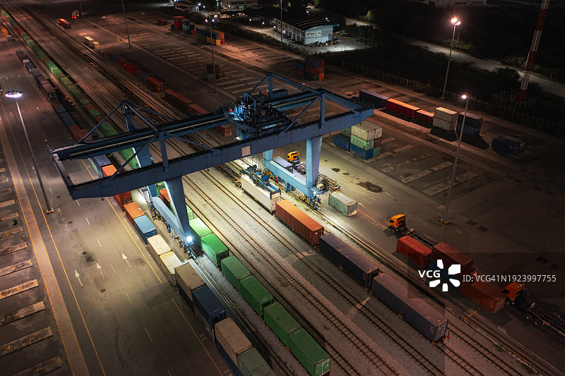 起重机在夜间从货运列车上装卸集装箱，用于商业物流、进出口运输或货运的鸟瞰图图片素材