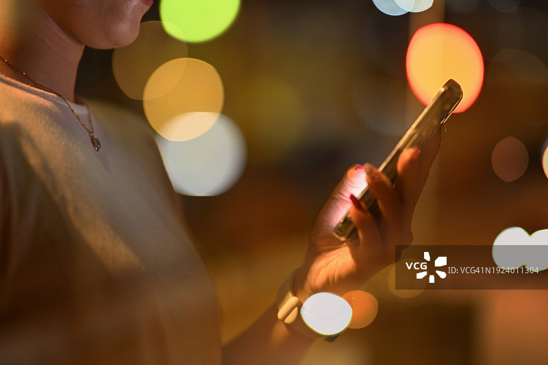 在城市夜景散景灯光下使用手机的女人图片素材