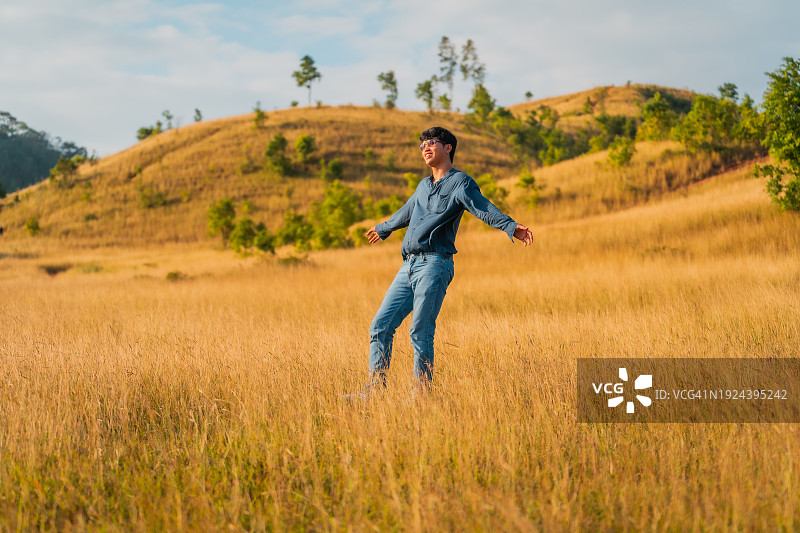 男子戴着太阳镜站在黄色田野上，背景是山图片素材