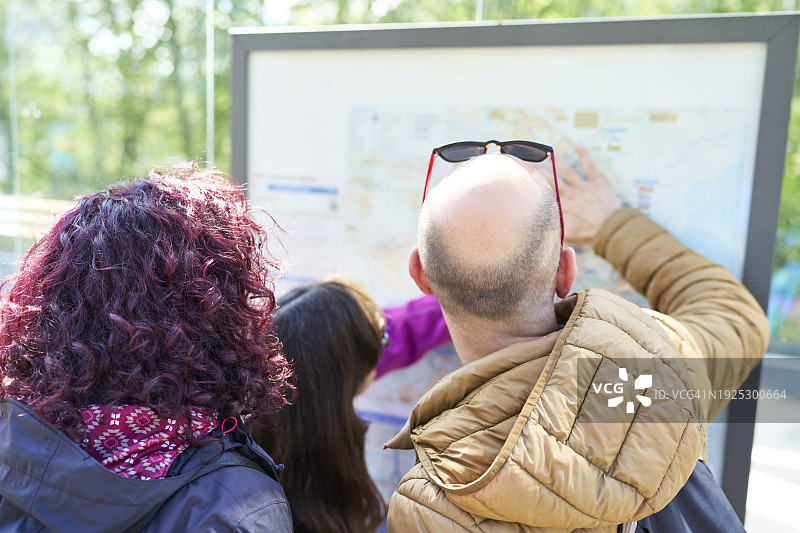 一群游客站在街上，看着广告牌上的地图的背影图片素材