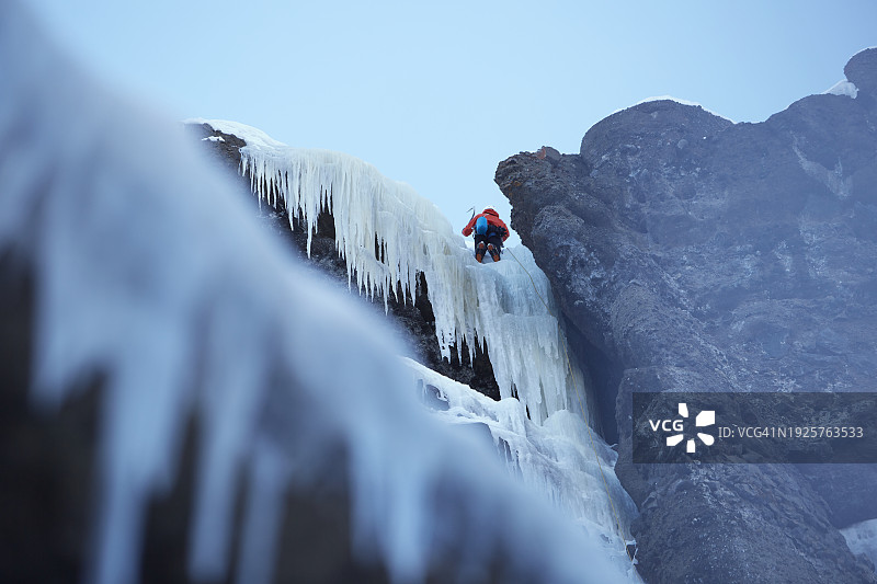 年轻男人在冬天攀登冰冻的瀑布悬崖图片素材