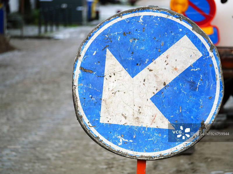 聚焦蓝色背景上带白色箭头的圆形金属板，布鲁塞尔施工街道旁的道路标志，阳光明媚图片素材