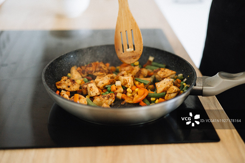 在家中，一位路人正在用平底锅烹饪肉类蔬菜图片素材