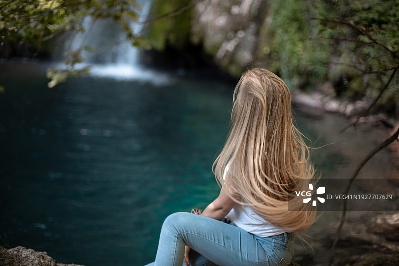 年轻女人坐在瀑布旁的自然环境中，长发飘逸图片素材