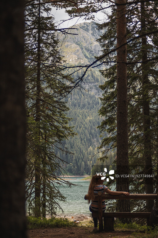 年轻女人在阳光明媚的日子里坐在木凳上，欣赏着山和湖的景色图片素材