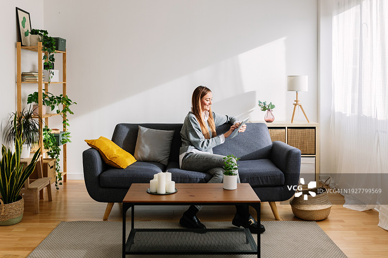 年轻女子在家中沙发上使用平板电脑放松图片素材