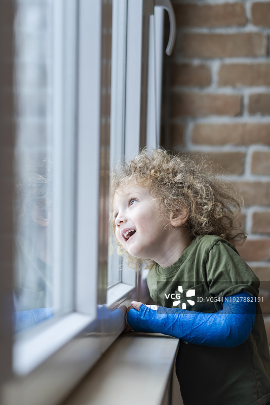 在家打着石膏的小男孩正在看窗外图片素材
