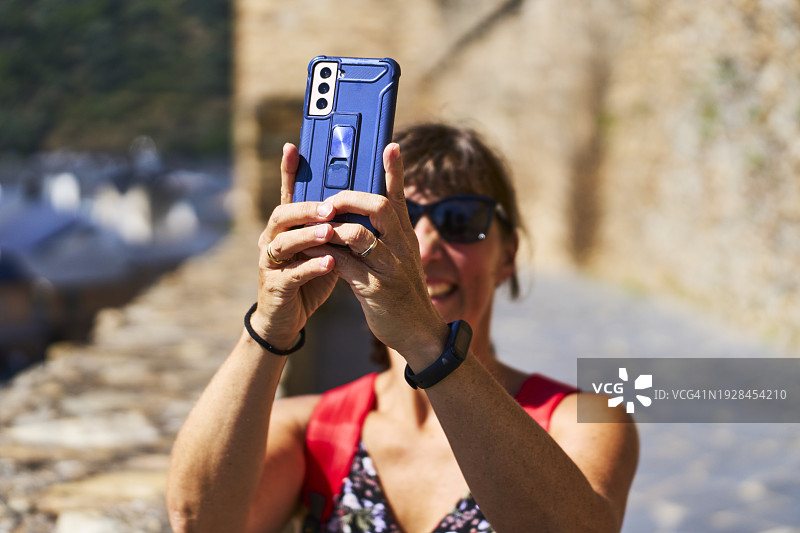 举起手臂用手机拍照，面带微笑，戴着墨镜的女人图片素材