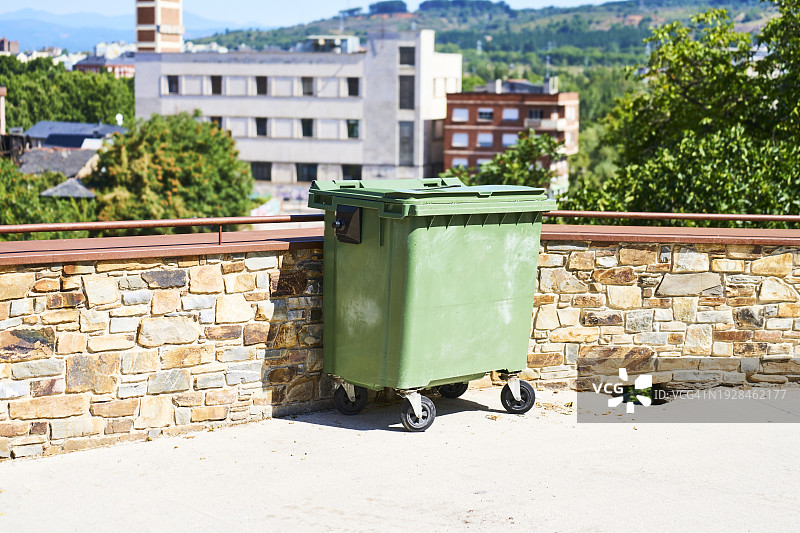 建筑物外侧的金属垃圾箱侧视图，背景是树木图片素材