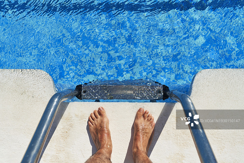 男子站在泳池边金属梯子上的高角度视图图片素材