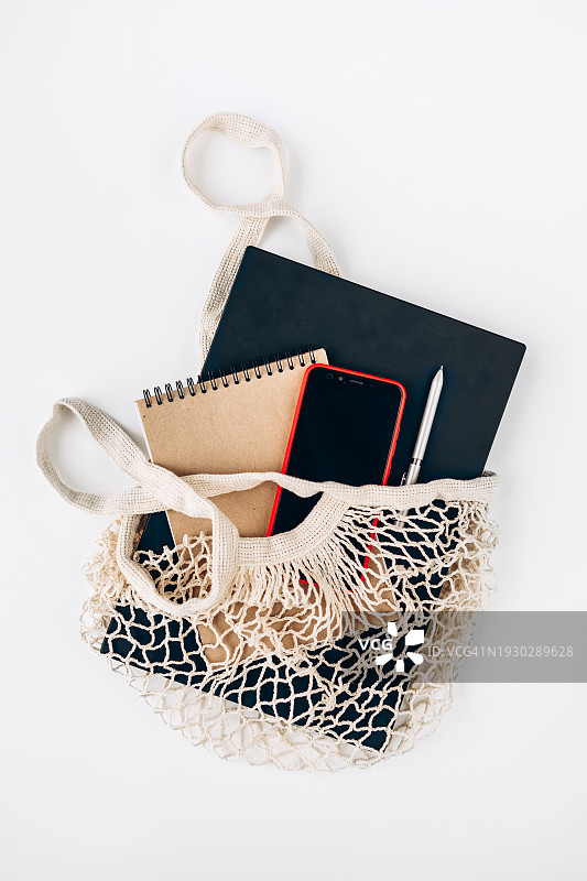 白色背景上的笔记本电脑、手机、笔记本和笔在可重复使用的购物袋中图片素材