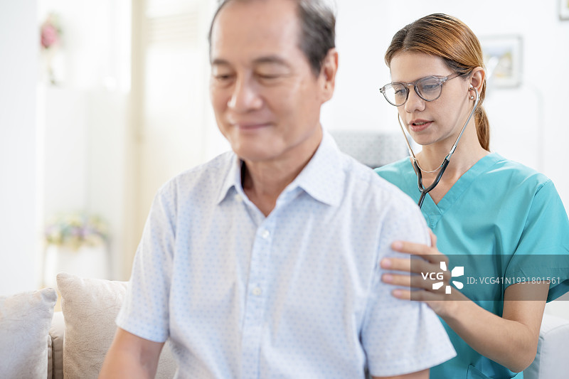 为预防老年疾病进行基础评估：居家护士在家访期间用听诊器检查男病人的背部，进行一般疾病评估图片素材